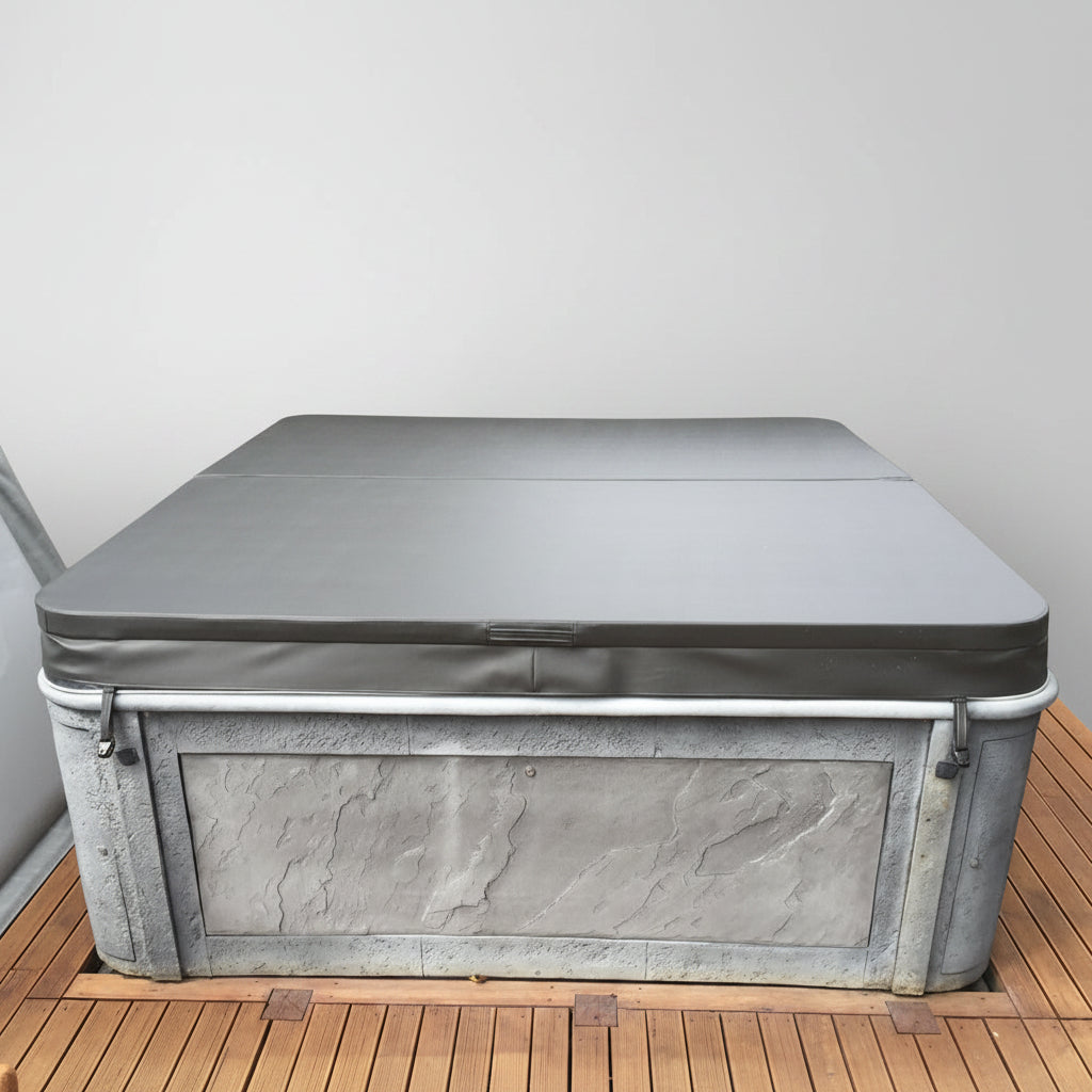 A gray protective cover for an outdoor hot tub or pool, secured over a gray metal tub on a wooden deck with a dark fence in the background.